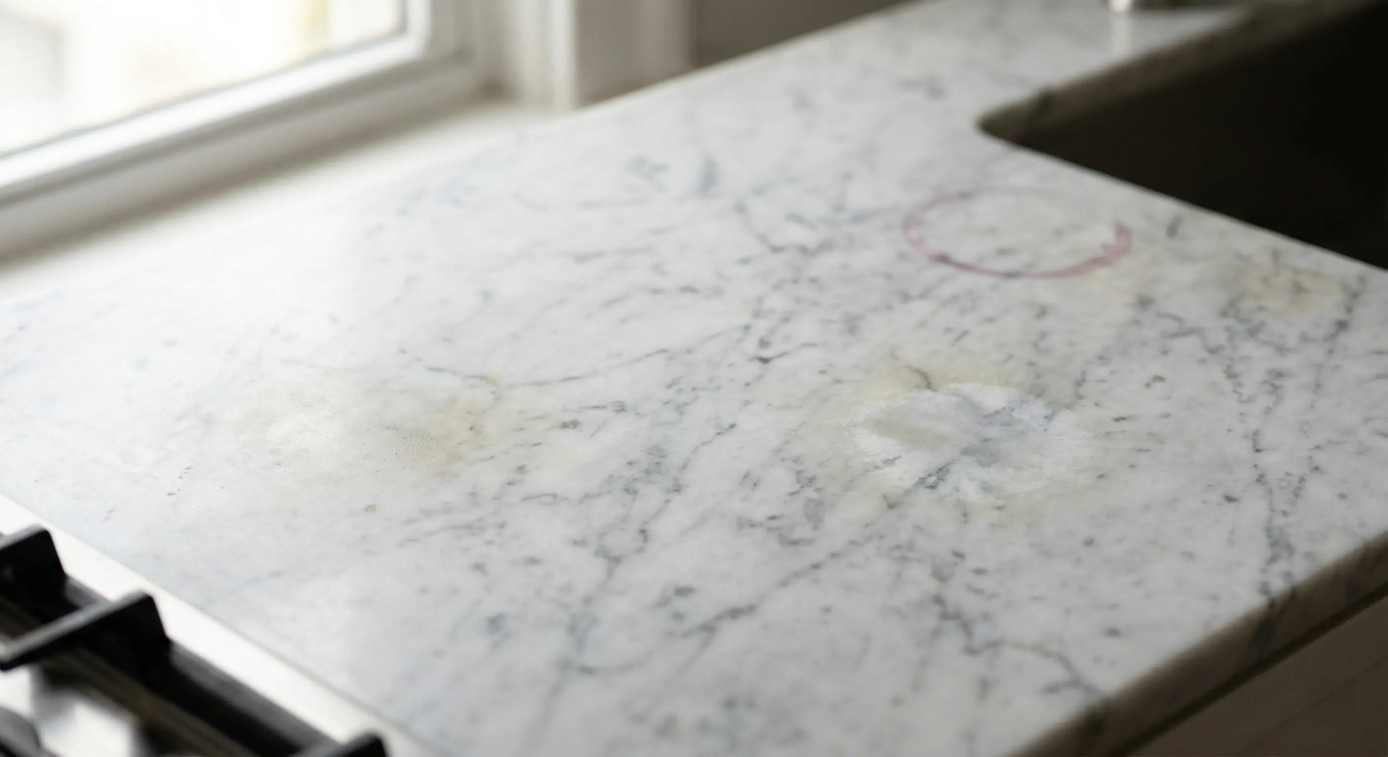 White marble kitchen countertop with etching stains and wear from cooking